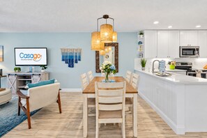A modern kitchen with white cabinets, a central island, and a dining area with a wooden table and chairs.