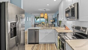 A modern kitchen with stainless steel appliances, white cabinets, and a central island. - Lovely ocean-view condo with pools, hot tubs, private W/D, & central AC (St. Augustine)