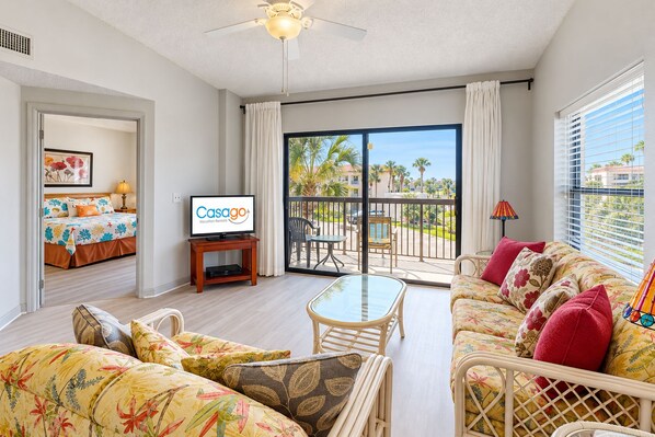 A spacious living room with a balcony, a television, and a bed with floral bedding.