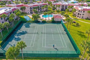 An aerial view of a tennis court surrounded by palm trees and a pool area, with a residential building in the background. - Dog-friendly condo with private beach, pools,tennis & gym (St. Augustine)