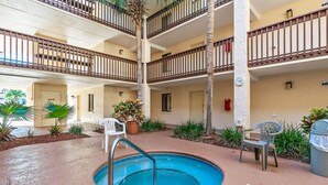 Zona de piscina interior con varios niveles, una piscina central rodeada de palmeras y plantas en macetas.