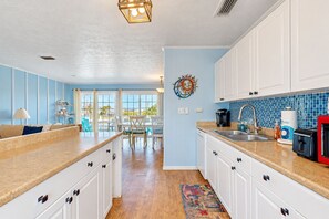 A kitchen with white cabinets, a blue backsplash, and a dining area with a view.