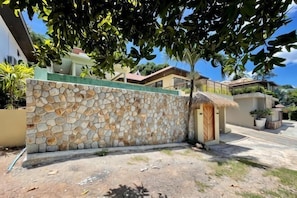 A stone wall, a thatched-roof structure, and a paved area with a tree overhead.