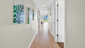 A hallway with a tiled floor, white walls, and a door at the end leading outside. - Newly decorated ground-floor suite steps from beach and pool w/views, WiFi (St. Augustine)