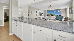 A kitchen with white cabinetry, a granite countertop, and a view of the outdoors. - Newly decorated ground-floor suite steps from beach and pool w/views, WiFi (St. Augustine)