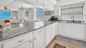 A kitchen with white cabinetry, granite countertops, and a view of the ocean through large windows. - Newly decorated ground-floor suite steps from beach and pool w/views, WiFi (St. Augustine)