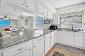 A kitchen with white cabinetry, granite countertops, and a view of the ocean through large windows.