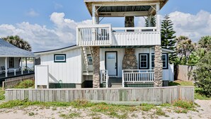 Une maison à deux étages située en bord de mer, dotée d’un balcon, de piliers en pierre et d’une clôture en bois.
