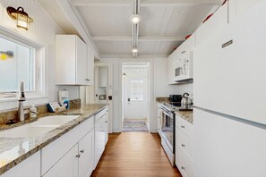Une cuisine moderne avec des meubles blancs, des comptoirs en granit, un évier en acier inoxydable, un four encastré et un four à micro-ondes.