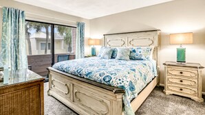 Quarto com uma cama grande, cômoda, mesa de cabeceira e janela com cortinas.