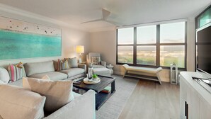 A modern living room with a large window, a ceiling fan, and a view of the cityscape. - First floor oceanfront condo with beach access and tennis courts (St. Augustine)