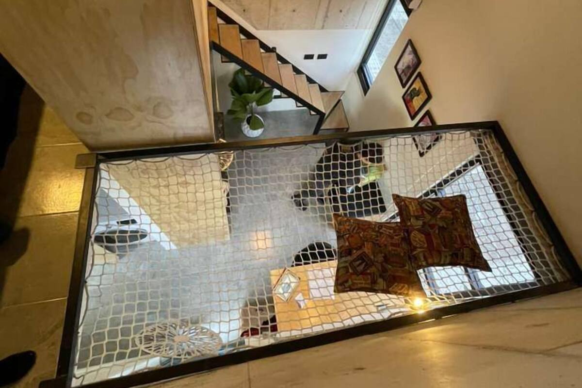 A staircase with a glass barrier, a hanging light fixture, and a plant on the landing.