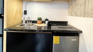 A compact kitchen with black cabinets, a built-in microwave, a sink, and a small refrigerator. - Living Universidad (Puebla)