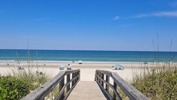 A wooden boardwalk leading to a beach with umbrellas and people. - Spacious condo with 2 private balconies, beach access and pool (St. Augustine)