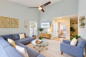 A modern living room with a sectional sofa, a glass coffee table, and a ceiling fan. - Spacious condo with 2 private balconies, beach access and pool (St. Augustine)