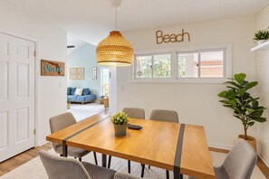A dining area with a wooden table, six chairs, a hanging pendant light, and a wall-mounted sign that reads 'Beach'. - Spacious condo with 2 private balconies, beach access and pool (St. Augustine)