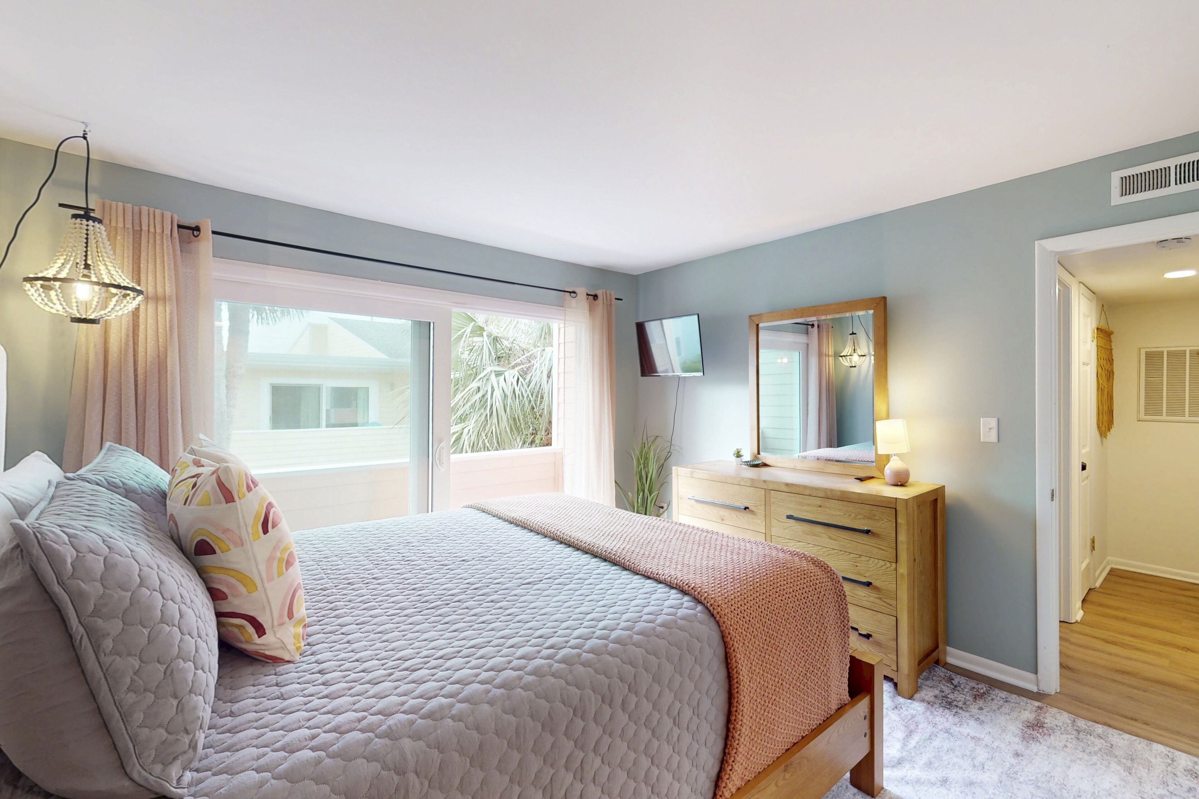 A bedroom with a bed, a dresser, a TV, and a window with curtains.