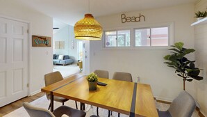 A dining area with a wooden table, chairs, a hanging light fixture, and a wall sign that reads "Beach". - Spacious condo with 2 private balconies, beach access and pool (St. Augustine)