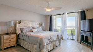 Ein Schlafzimmer mit Bett, Nachttisch, Lampe, Fernseher und Blick ins Freie.