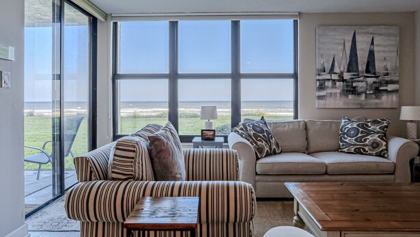 Ein Wohnzimmer mit großem Fenster, Deckenventilator, einer Couch, einem gestreiften Sessel und einem Holztisch.