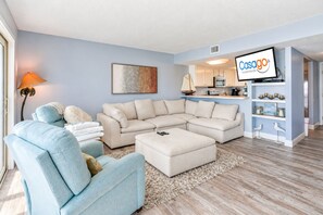 A modern living room with a sectional sofa, a small round table, and a TV mounted on the wall.