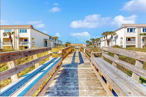 A wooden boardwalk leading to a beachfront property with multiple-story buildings, each featuring balconies and a clear view of the ocean. - Modern Ocean View Home with Pool, Pickleball, and Beach Access (St. Augustine)