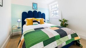 Une chambre à coucher avec une tête de lit bleue, une couvre-lit matelassée, une petite table de chevet avec une lampe et une fenêtre donnant sur un beau paysage.