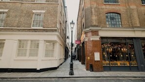 Une rue étroite, bordée de bâtiments des deux côtés, dont une boutique avec de grandes vitrines et une enseigne.