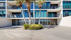 A modern hotel with multiple balconies, palm trees, and a concrete courtyard.