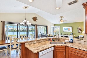 A kitchen with granite countertops, a dishwasher, and a dining area with chairs and a table.