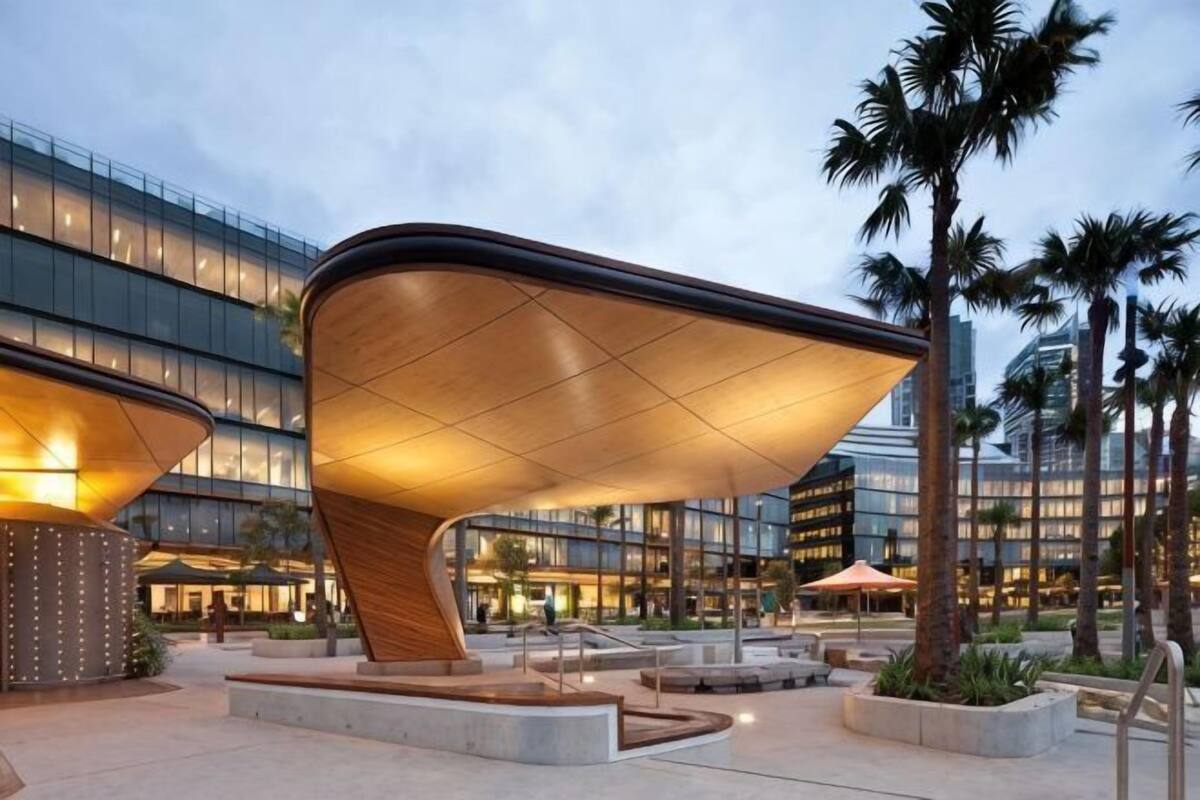 A modern building with a unique curved roof structure, surrounded by palm trees and a well-lit plaza.