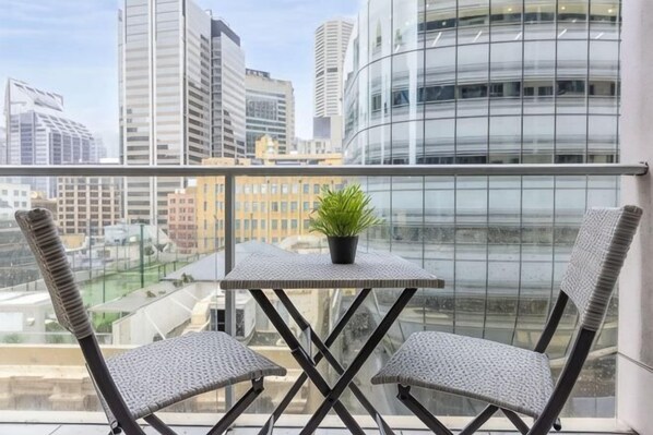 A balcony with a table and two chairs, a potted plant, and a city view. - A Cozy Studio CBD Next to Darling Harbour (Sydney)