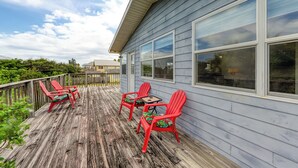Een houten terras met rode Adirondack-stoelen en een kleine tafel.