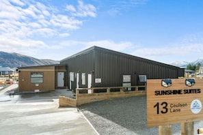 A building with a sign for Sunshine Suites at 13 Coulson Lane, featuring a large entrance and a parking area. - Sunshine Suites (Lake Tekapo)