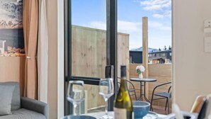 Una habitación moderna con un ventanal grande, un sofá, una mesa de comedor con copas de vino y una botella, y vistas a edificios y montañas.