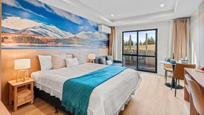 Habitación de hotel moderna con una cama grande, un escritorio y vistas a un paisaje montañoso por la ventana.