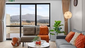 Una sala de estar moderna con un sofá, una mesita redonda con fruta y un amplio ventanal con vistas a la montaña.