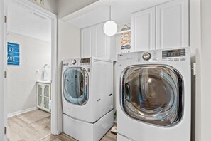 A laundry room with two front-loading washing machines and a cabinet with a towel hanging on it. - Colorful condo w/shared pool, free WiFi, central A/C - blocks from the beach (St. Augustine)