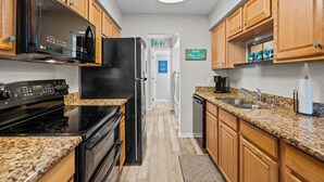 A compact kitchen with granite countertops, black appliances, wooden cabinets, and a visible laundry area. - Colorful condo w/shared pool, free WiFi, central A/C - blocks from the beach (St. Augustine)