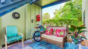 A covered porch with a wicker sofa, a chair, a bicycle, and a potted plant. - Colorful condo w/shared pool, free WiFi, central A/C - blocks from the beach (St. Augustine)