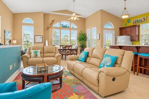 A spacious living room with a beige sofa, a coffee table, and a dining area with a table and chairs. - Two-level home with partial ocean view, balcony, WiFi, & W/D - walk to the beach (St. Augustine)