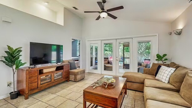 A spacious living room with a large flat-screen TV, a wooden coffee table, a brown leather sofa, and a ceiling fan. - Dog-Friendly home with enclosed backyard, private hottub and sunroom (St. Augustine)