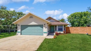A two-story house with a green garage door, a front porch with a potted plant, and a wooden fence. - Dog-Friendly home with enclosed backyard, private hottub and sunroom (St. Augustine)