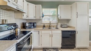 A modern kitchen with white cabinets, a stove, microwave, toaster, sink, and dishwasher. - Dog-Friendly home with enclosed backyard, private hottub and sunroom (St. Augustine)