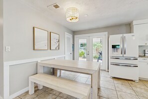A modern kitchen with white cabinetry, a built-in oven, and a refrigerator. There is a wooden bench and two framed artworks on the wall.