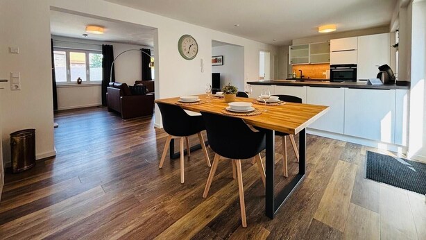 A modern kitchen with a dining area, wooden flooring, and a clock on the wall.