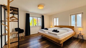 A bedroom with a wooden bed, a desk, a chair, and a window with curtains.