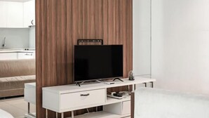 A modern living room with a flat-screen TV on a white console, a wooden accent wall, and a minimalist design. - Mansion One Suites by Simply Penang (George Town)