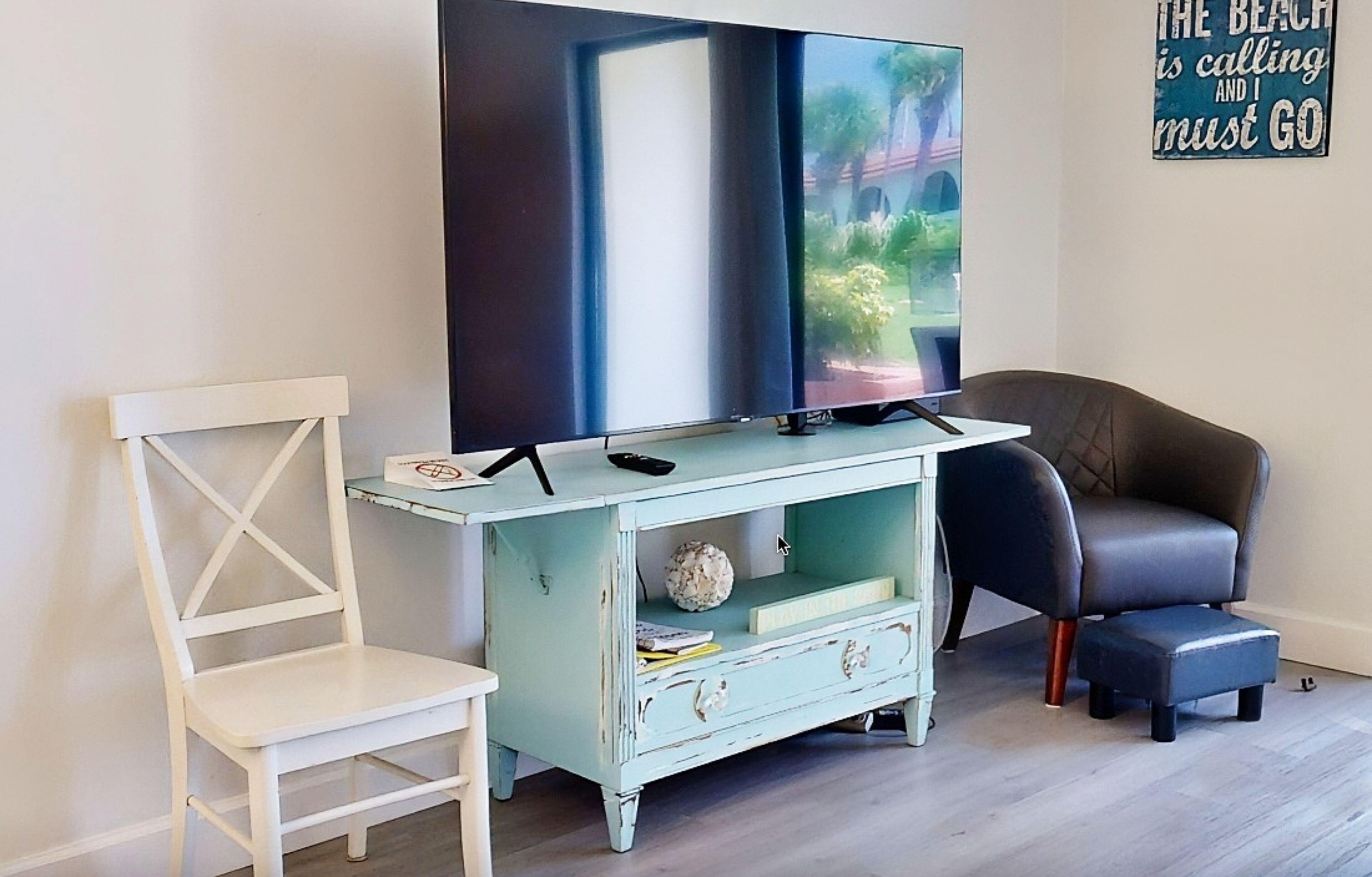 Una sala de estar con televisor, una silla blanca, un aparador azul y un sillón de cuero negro.