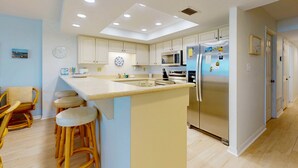 A modern kitchen with white cabinets, a central island with stools, a stainless steel refrigerator, and a microwave. - Oceanfront condo with pool, ocean views, and washer/dryer (St. Augustine)